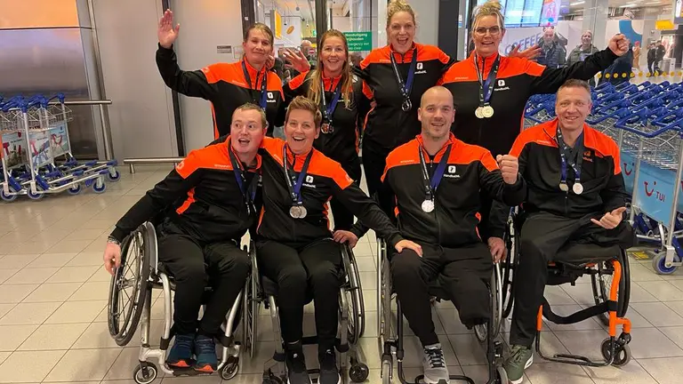 Het Nederlands rolstoelhandbalteam met zilveren medailles op de luchthaven na het EK/WK.