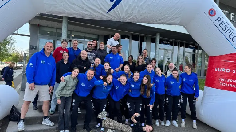 Groepsfoto onder de Limburg Handball Cup-boog met speelsters, begeleiders en ouders van de MB2/C1.