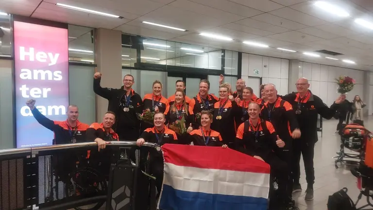 Het Nederlands rolstoelhandbalteam viert de zilveren medailles met een Nederlandse vlag op Schiphol.